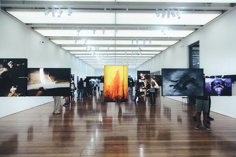 A contemporary art gallery with visitors observing various photographic exhibitions displayed on walls and stands.